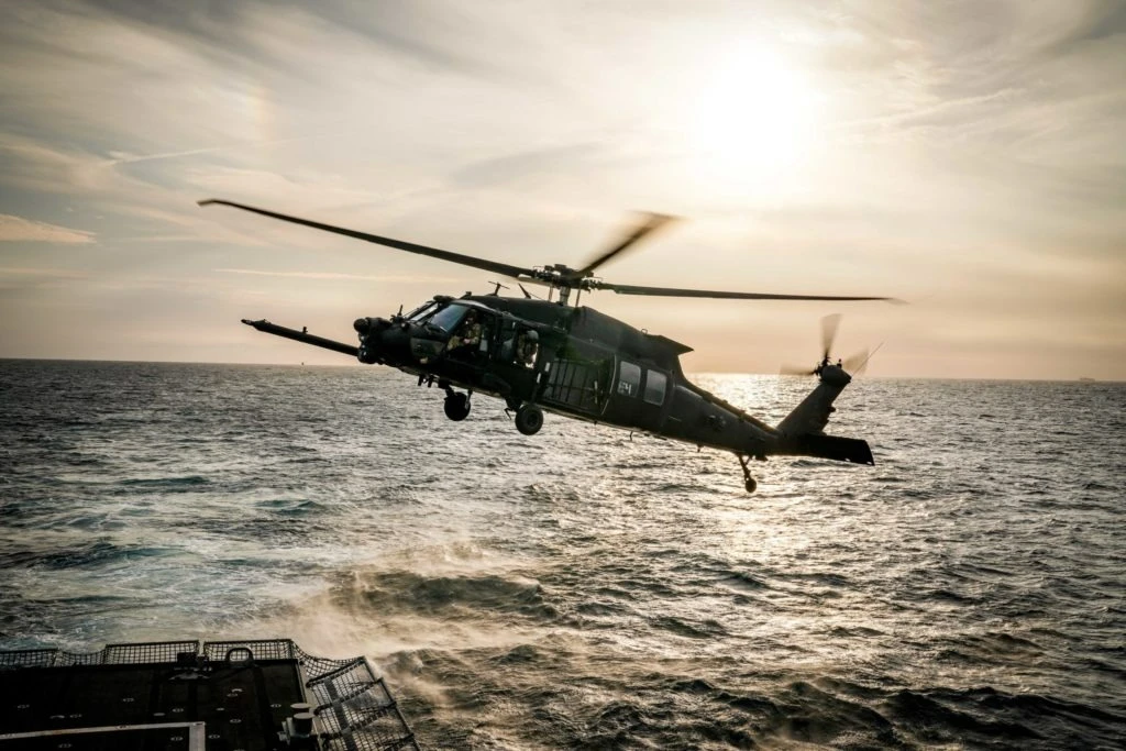MH-60 Black Hawk over sea next to ship deck at sunset